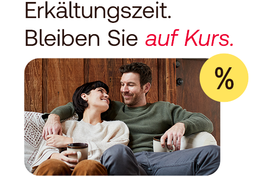 A couple sitting on the sofa drinking tea and smiling at each other.