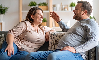 Zwei Menschen sitzen lächelnd auf dem Sofa und führen ein entspanntes Gespräch.
