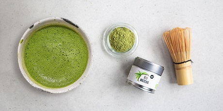 Thé matcha dans un bol, poudre de matcha dans un verre, boîte et fouet en bambou.