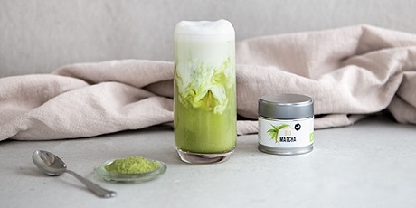 Verre de boisson au matcha, boîte, poudre de matcha sur une assiette et cuillère.