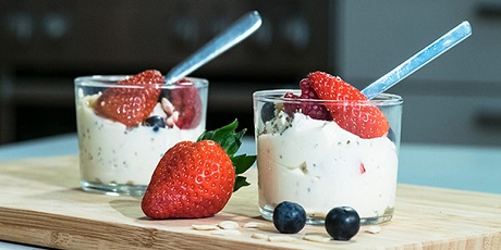 Deux verres avec dessert, fraises et myrtilles. Sur une planche en bois. Une fraise et deux myrtilles sont à côté.